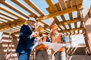mature businessman near builders in helmets holding blueprint
